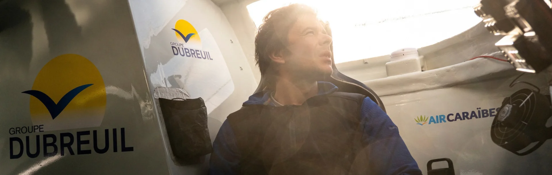 Sébastien Simon, à l'intérieur de son cockpit, regarde par le hublot sous un soleil couchant