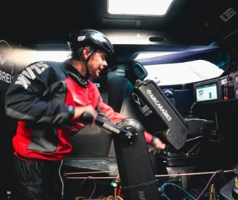 À bord de l'IMOCA Groupe Dubreuil 2, Sébastien Simon mouline au winch dans le cockpit, devant les écrans de navigation.