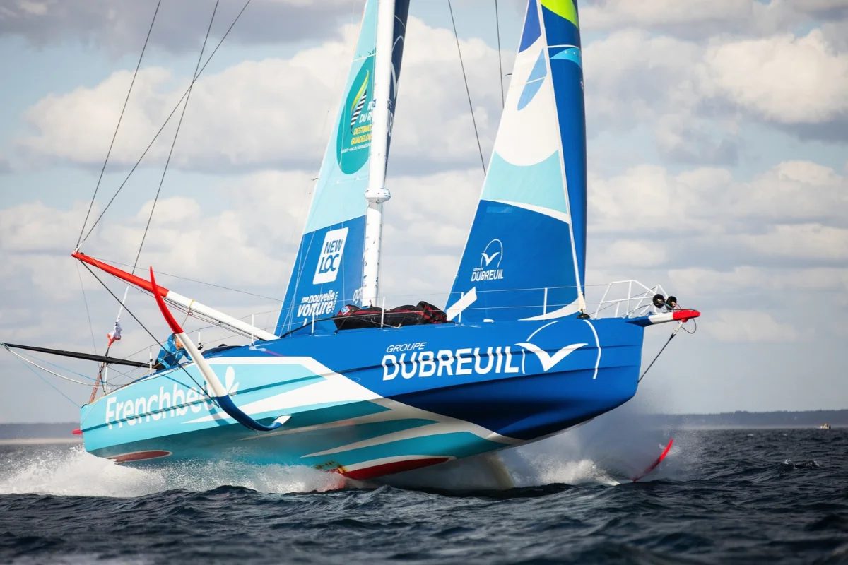 L'IMOCA Groupe Dubreuil 2 s'élève au-dessus de l'eau sur ses foils en soulevant des gerbes d'écume.