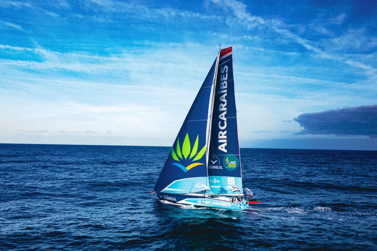 L'IMOCA Groupe Dubreuil 2 navigue au près sur l'océan, sa grand-voile et son foc arborant les logos Air Caraïbes et Groupe Dubreuil sous un ciel bleu.